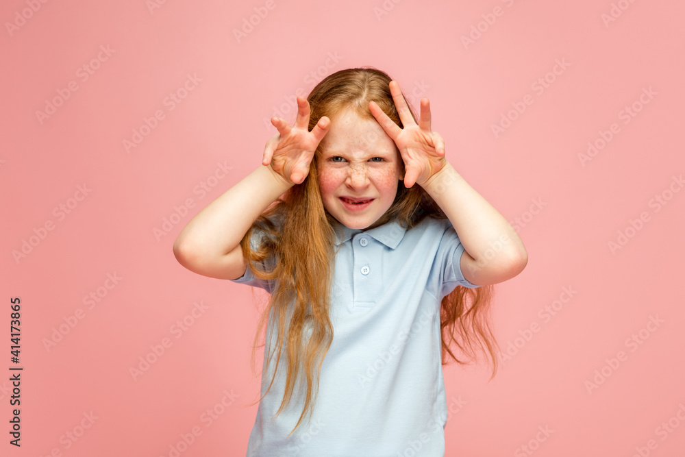 Wall mural peek-a-boo, gremaces. happy, smiley redhair girl isolated on pink studio background with copyspace f