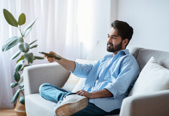 Arab man with remote controller switching channels while watching tv at home