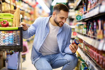 Young smiling guy with the cart shopping in hypermarket