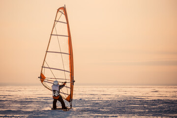 Winter windsurfing. Man riding a surf in the snow at sunset. Extreme winter sport. The rear view
