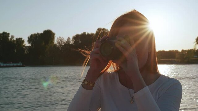 [4k] backlit model in front of water with sunstar behind her head taking photos with a vintage slr camera