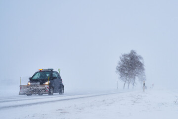 Kleiner lustiger Schneepflug auf Schneebedeckter Straße bei Schneesturm im Winter