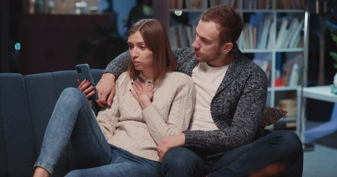 Caucasian couple of wife and husband communicasting online on mobile phone videocall. Unhappy young woman learning bad news talking webcam wirh family.