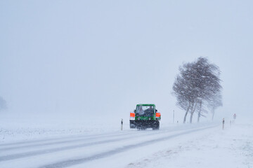 Schneepflug auf Schneebedeckter Straße bei Schneesturm im Winter