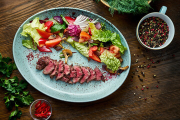 Warm salad with medium rare beef and fresh vegetables, served in a blue plate on a wooden background. Restaurant food. Close up, selective focus