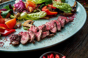 Warm salad with medium rare beef and fresh vegetables, served in a blue plate on a wooden background. Restaurant food. Close up, selective focus