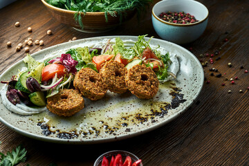 Appetizing salad in the style of oriental cuisine. Fresh vegetable salad with falafel and olive oil served in a blue plate on a wooden background. Restaurant food