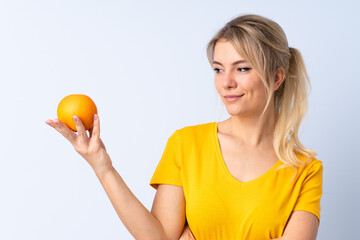 Blonde woman over isolated blue background holding an orange