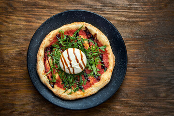 Wood-fired pizza with burrata, arugula, red sauce and balsamic with crispy sides, served on a black plate on a wooden background. pizzette a kind of Italian pizza