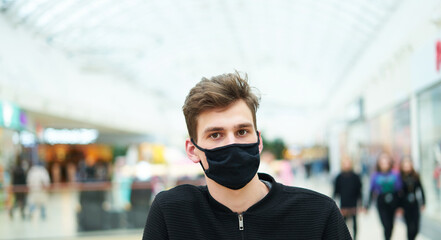 Fototapeta na wymiar Portrait of young man in medical mask in store, modern mall