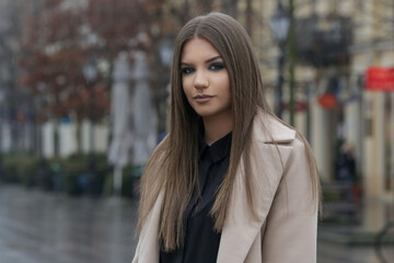 Outdoor portrait of young stylish woman in camel coat in the city on a rainy day