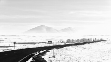 Misty winter scene on a rural road with hills in the background