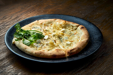 Wood-fired pizza with 4 types of cheese and white sauce with crispy sides, served on a black plate on a wooden background. pizzette a kind of Italian pizza