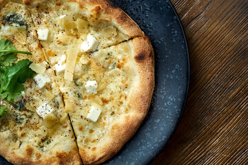 Wood-fired pizza with 4 types of cheese and white sauce with crispy sides, served on a black plate on a wooden background. pizzette a kind of Italian pizza