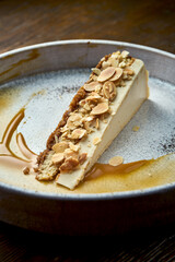 Classic slice of cheesecake with almonds and caramel sauce, served in a white plate on a wooden background. Restaurant food. Appetizing dessert