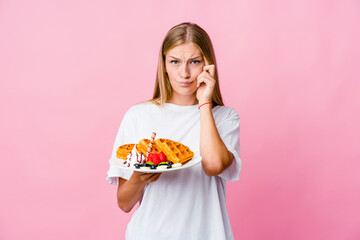 Young russian woman eating a waffle isolated focused on a task, keeping forefingers pointing head.