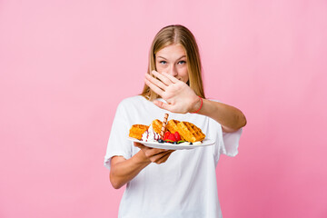 Young russian woman eating a waffle isolated doing a denial gesture