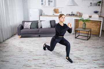 Obraz premium A young slender girl goes in for sports at home, she is dressed in fitness clothes, a black top and leggings. Fitness at home for a beautiful body