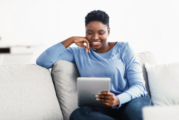 Black woman sitting on couch and using digital tablet
