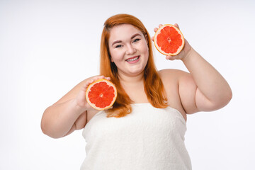 Overweight young woman in spa towel holding grapefruits isolated in white
