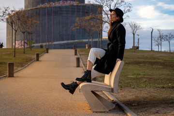 Fototapeta na wymiar Chica con sombrero y abrigo negro posando en el parque en una tarde de invierno