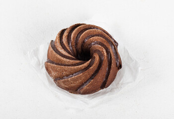 Chocolate round cake with icing on paper on a white background