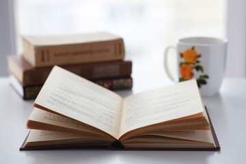 Old books, glasses, pencil and cup of coffee on white table background against window light with copy space