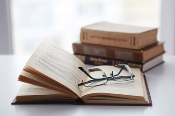 Old books, glasses, pencil and cup of coffee on white table background against window light with copy space