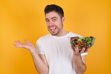 So what? Portrait of arrogant young handsome Caucasian man holding a salad bowl against yellow wall...
