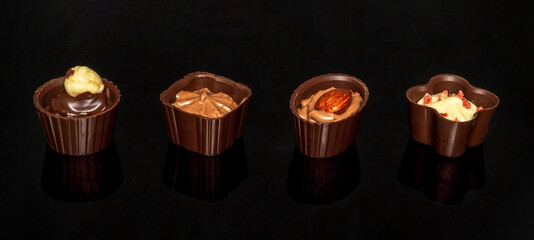 Sweets with cream and nuts on a black table. Assorted chocolate on black isolated background