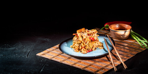 Thai vegetarian vegetables udon noodles in a dark background. Serving Asian dishes in the restaurant in a plate on a bamboo mat