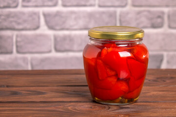 Jar of canned sweet red bell pepper on a wooden background against a gray wall with copy space
