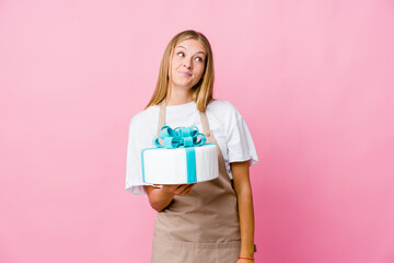 Young russian baker woman holding a delicious cake dreaming of achieving goals and purposes