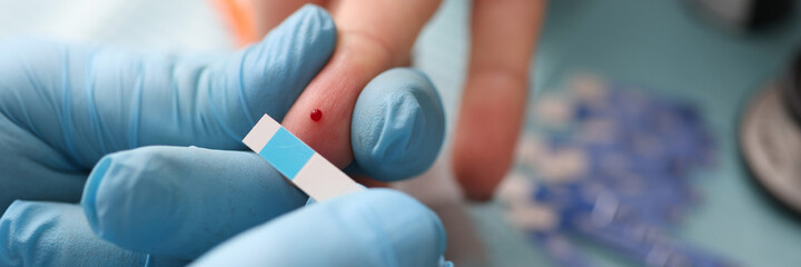 Doctor holding test strip near patients finger with drop of blood in clinic closeup. Glucometry in...