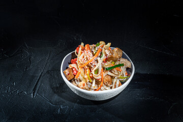 Udon stir-fry noodles with chicken and vegetables on dark background. Appetizing asian cuisine