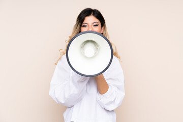 Teenager girl isolated on beige background shouting through a megaphone