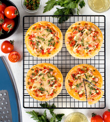 Mini pizzas with sausage, pickles, tomatoes, mozzarella, parsley on a metal stand on a light background top view 