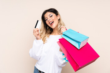 Teenager girl isolated on beige background holding shopping bags and a credit card