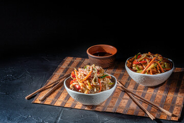 Udon noodles with fried chicken, shrimps (prawns) and vegetables on dark background