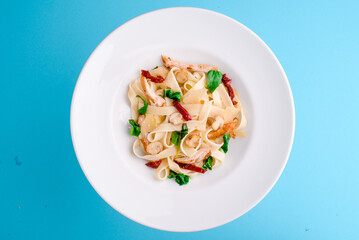 tagliatelle pasta with chicken, mushrooms and sun-dried tomatoes on a white plate on a blue background. close-up. photo for clipping. for the menu