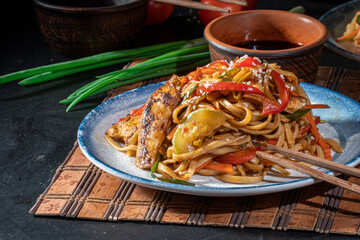 Udon stir-fry noodles with chicken and vegetables on dark background. Appetizing asian cuisine