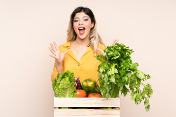 Teenager farmer girl with freshly picked vegetables in a box isolated on beige background unhappy and frustrated with something