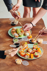 Sushi set on table in office. Party of friends eating sushi rolls using bamboo sticks. Corporate