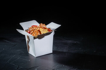 Udon noodles in white carton takeaway delivery box with vegetables and beef in teriyaki sauce. Asian food, and wooden sticks on dark background. The concept of fast food
