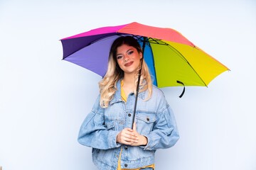 Teenager russian girl holding an umbrella isolated on blue background smiling a lot