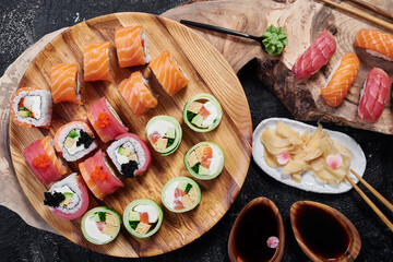Sushi set with Philadelphia, roll with avocado and roll with tuna on round wooden board on dark background. Close-up. Top view 