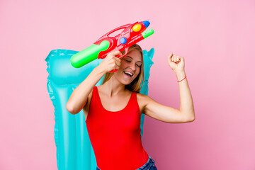 Young russian woman playing with a water gun with an air mattress celebrating a special day, jumps and raise arms with energy.