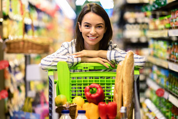 Young cheerful woman shopping in supermarket with trolley cart