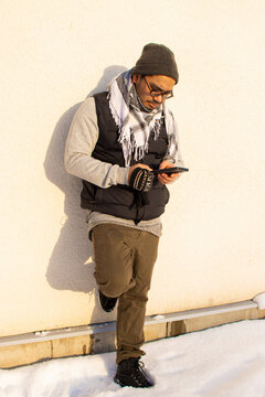 Man standing alone against a wall with a cell phone in his hand working online far from the office. sun and winter time