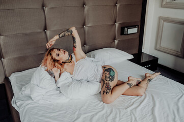 Portrait of a happy beautiful girl with tattoos. The woman is lying in bed.